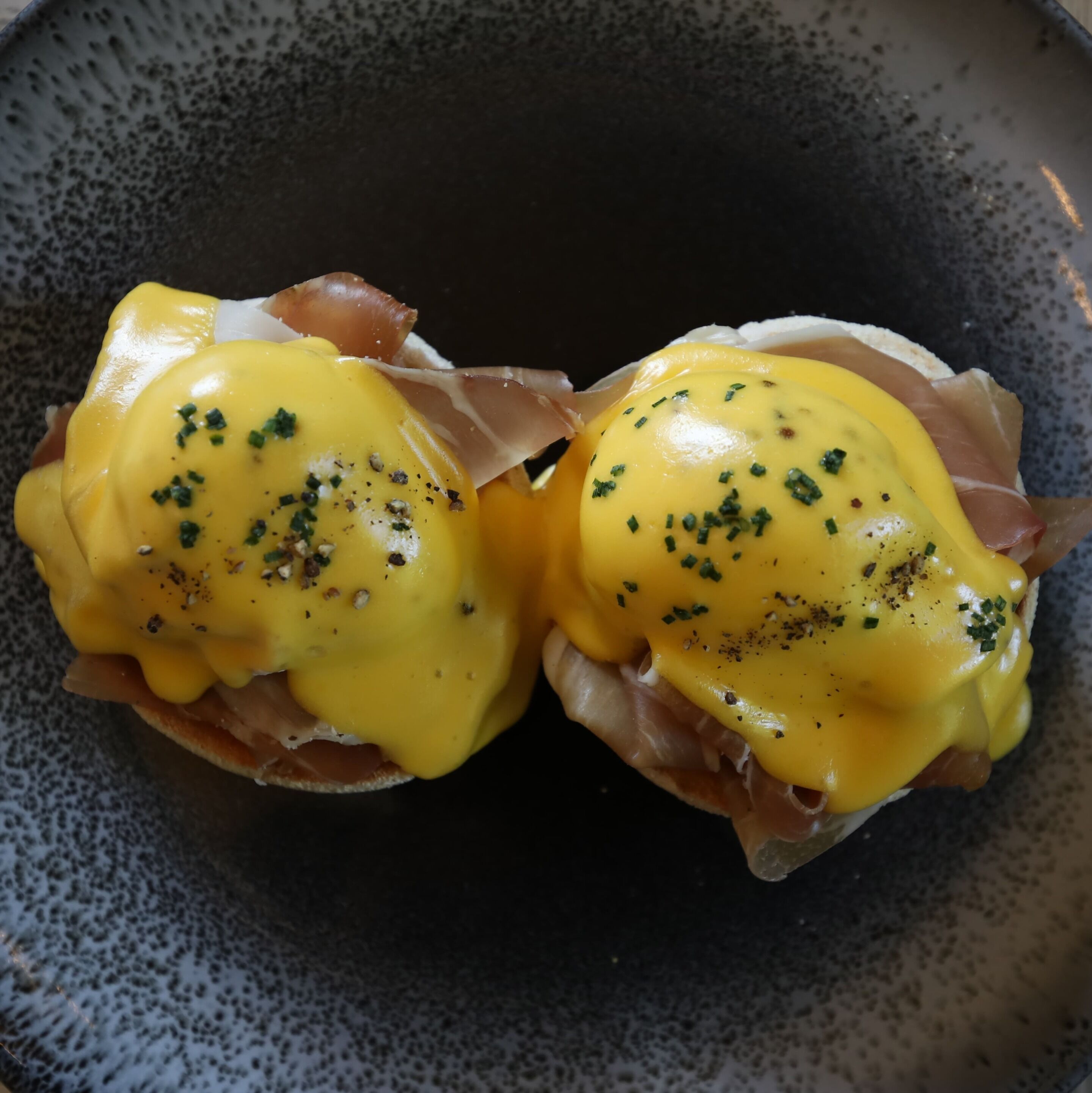 Dos sándwiches huevos benedictinos sobre un plato moteado.