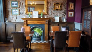 A restaurant with a stone wall, wooden furniture, and framed pictures. - The Hampton Hotel by Greene King Inns (Edinburgh)