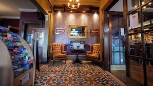 A lobby with a patterned floor, two leather armchairs, a table with a mirror, and a display of books. - The Hampton Hotel by Greene King Inns (Edinburgh)