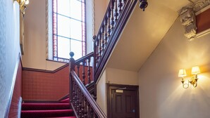 A grand staircase with red carpeted steps, a wooden handrail, and a large arched window with stained glass. - The Hampton Hotel by Greene King Inns (Edinburgh)