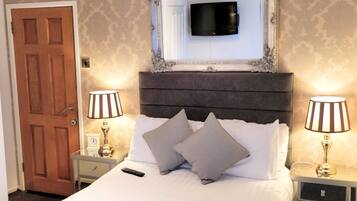 A hotel room with a large bed, two bedside tables with lamps, a television mounted above the bed, and a door to the left.