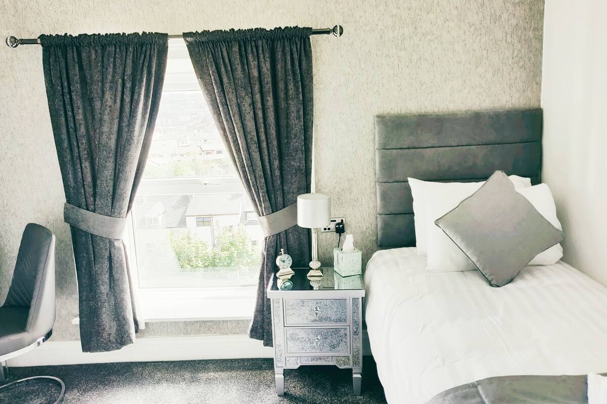 A hotel room with a bed, a nightstand, a chair, and curtains.