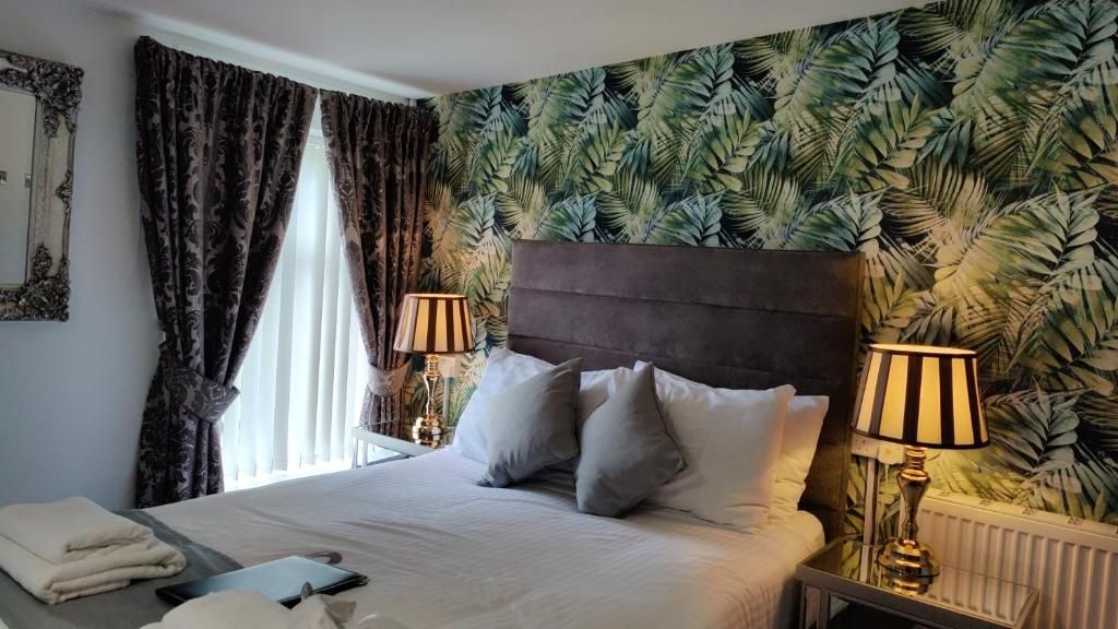 Een hotelkamer met een bed, twee bedlampen, een raam met gordijnen en een wand met een tropisch bladmotief.