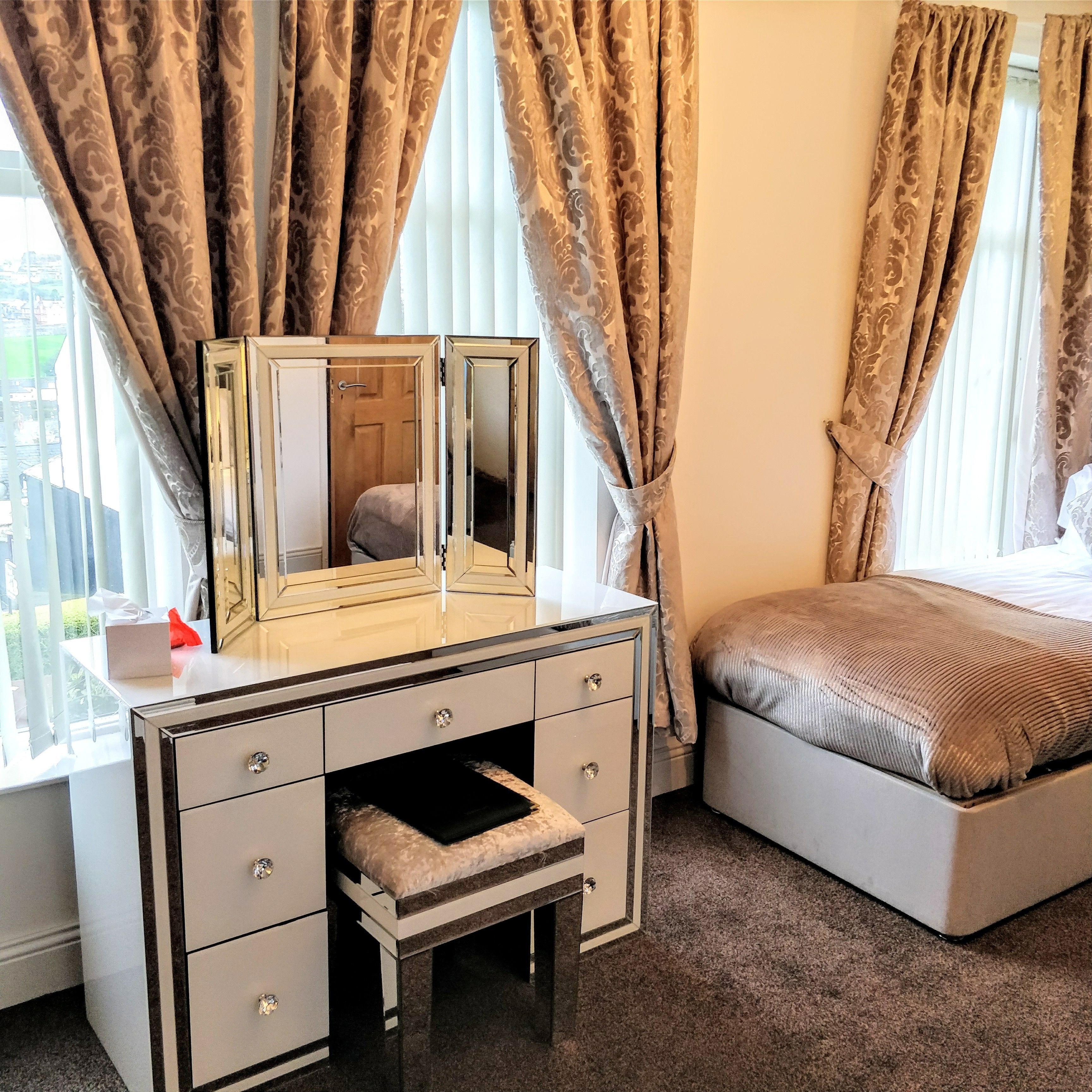 A hotel room with a vanity, a bed, and a window with curtains.