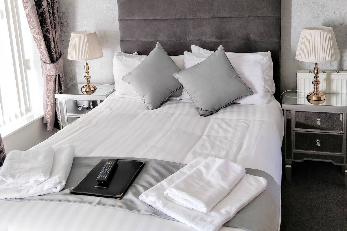 A neatly made bed with pillows, a remote control, and a book on a bedside table.
