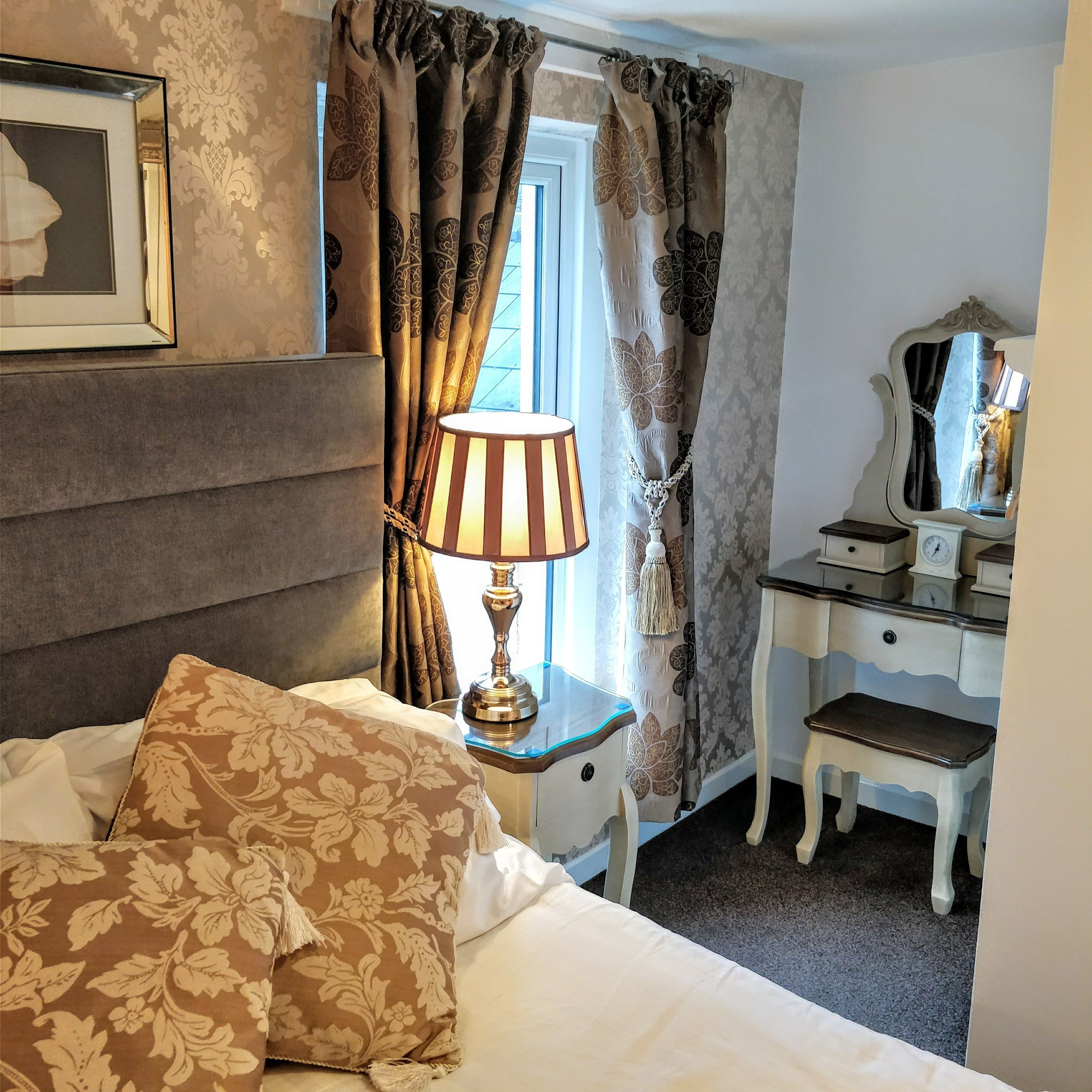 A bedroom with a bed, a nightstand with a lamp, a dresser, and a mirror.