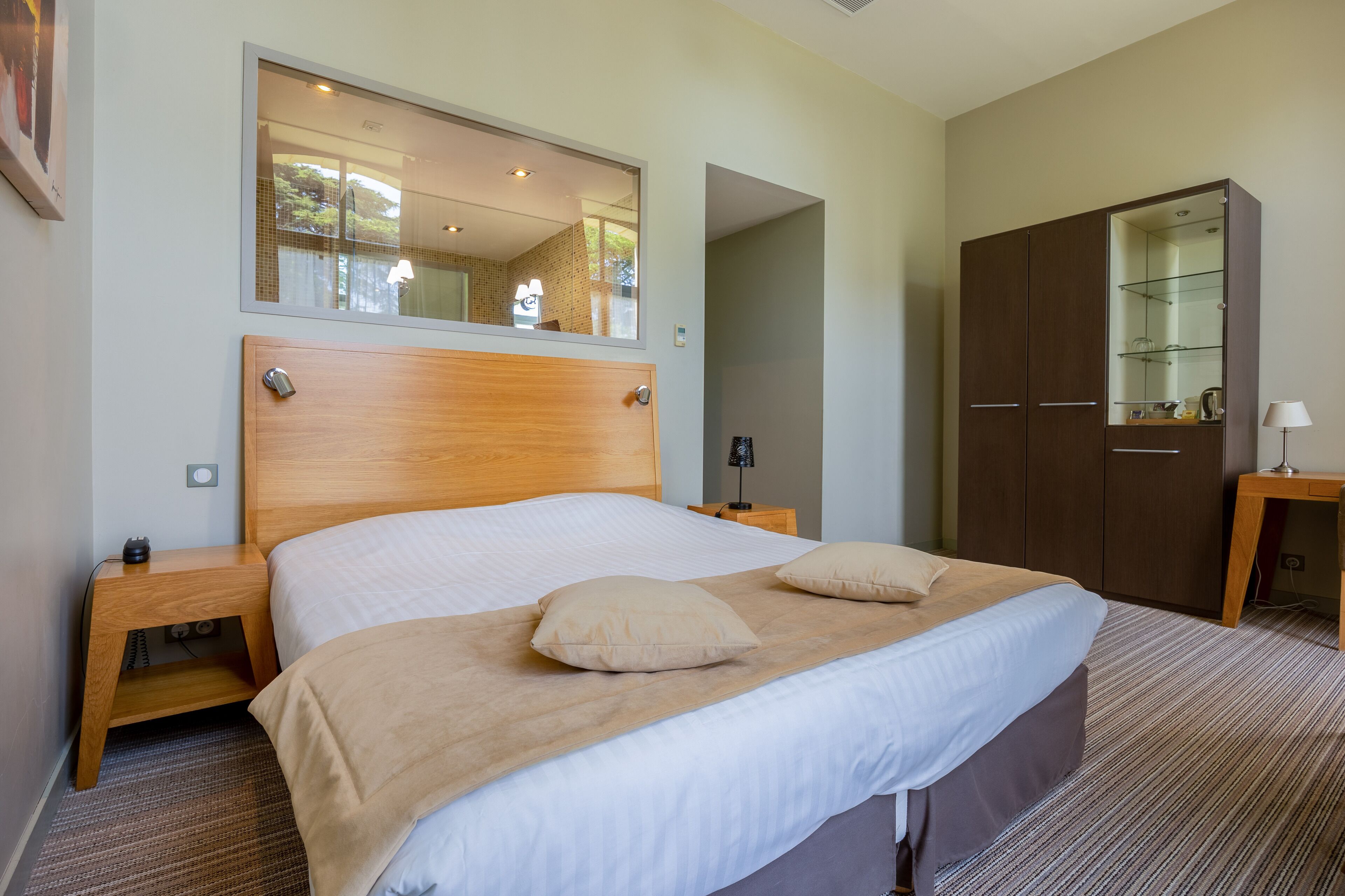 Una cama bien hecha con cabecera de madera, una mesita de noche con lámpara y un armario con espejo.