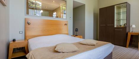 A neatly made bed with a wooden headboard, a bedside table with a lamp, and a wardrobe with a mirror.