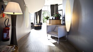 A modern hotel lobby with a sofa, a fire extinguisher, a lamp, and a potted plant.