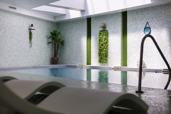 Una piscina interior con pared de azulejos, una planta en maceta y un reloj fijado a la pared.