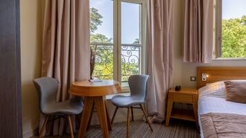 A hotel room with a bed, a small table, two chairs, a nightstand, and a window with curtains.