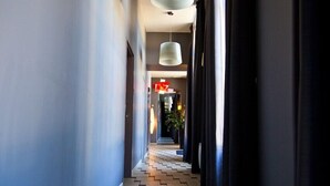 A narrow hallway with a zigzag patterned floor, leading to a room with a large window and a hanging light fixture.