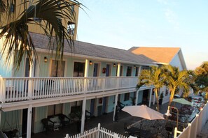 A hotel with a balcony, outdoor seating, and palm trees.
