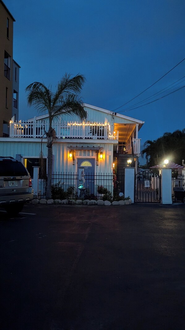 A two-story building with a white facade, a gated entrance, and a palm tree in the foreground.