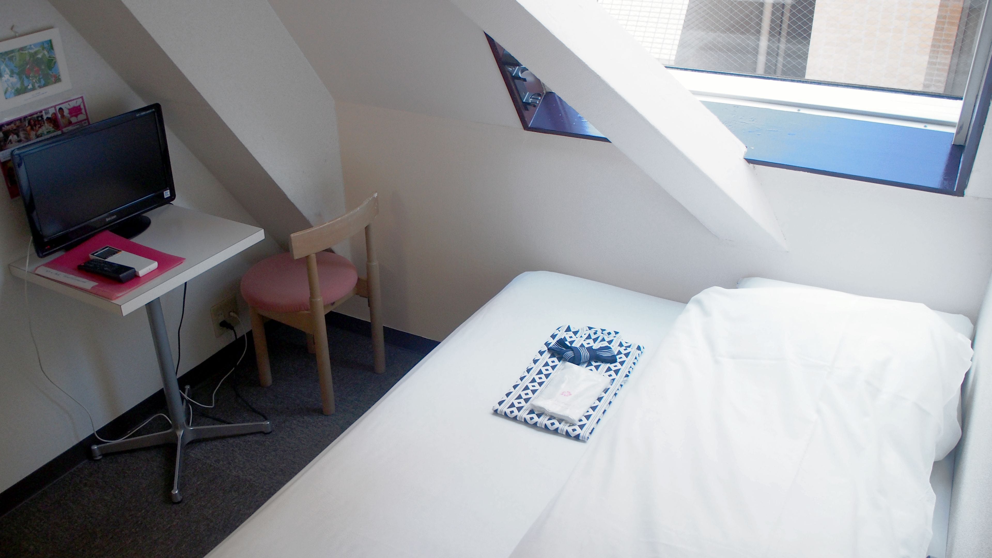 A small, compact room with a bed, a desk with a computer, and a chair.
