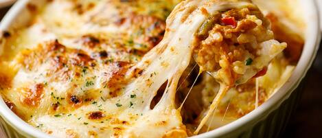 Gros plan d’un plat cuit au four, recouvert de fromage fondu et d’herbes, servi dans un plat en céramique.