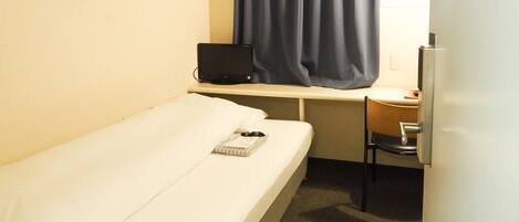 A small, single-bed room with a desk, chair, and a computer.