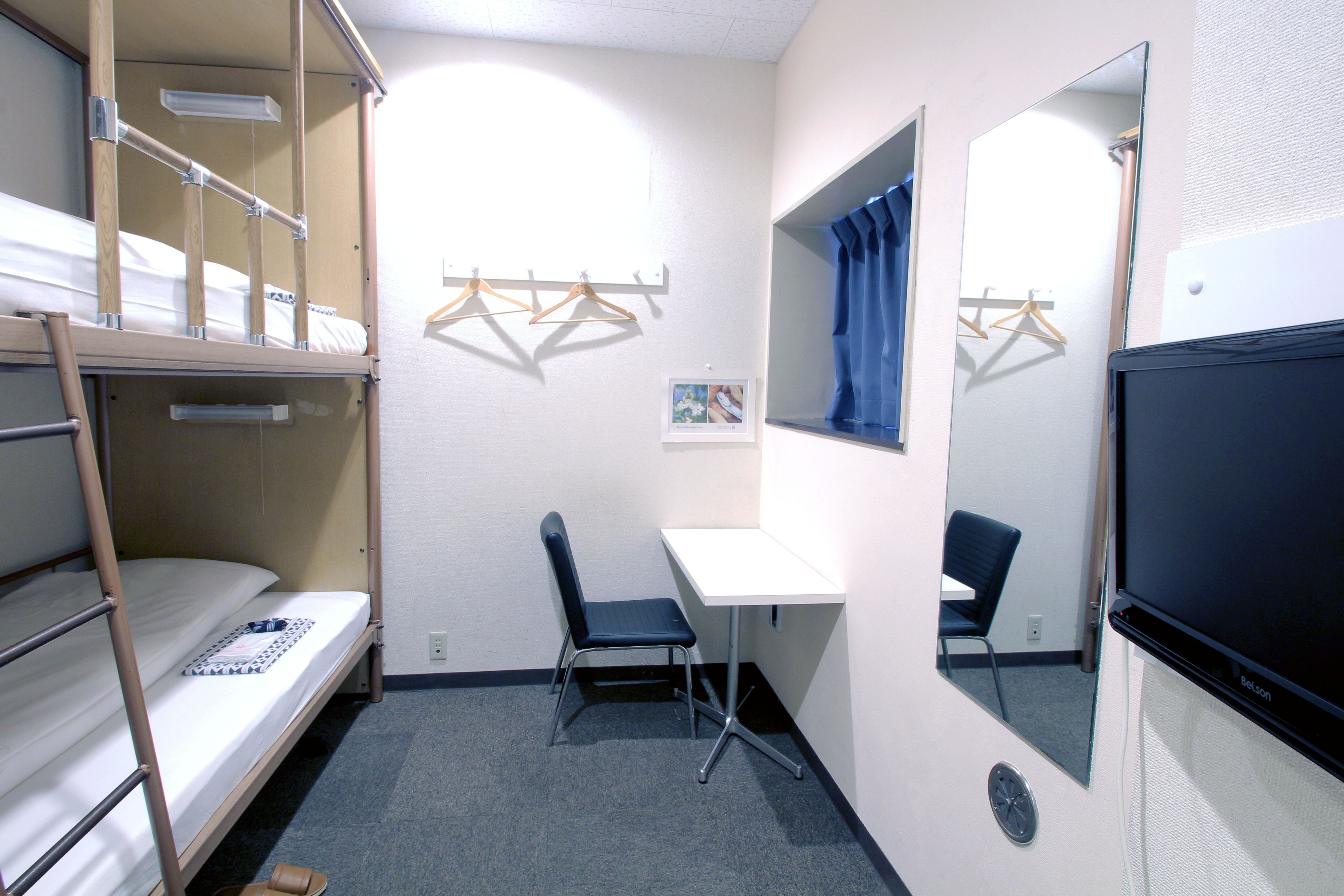 A bunk bed, a desk, a chair, a mirror, and a television in a small room.