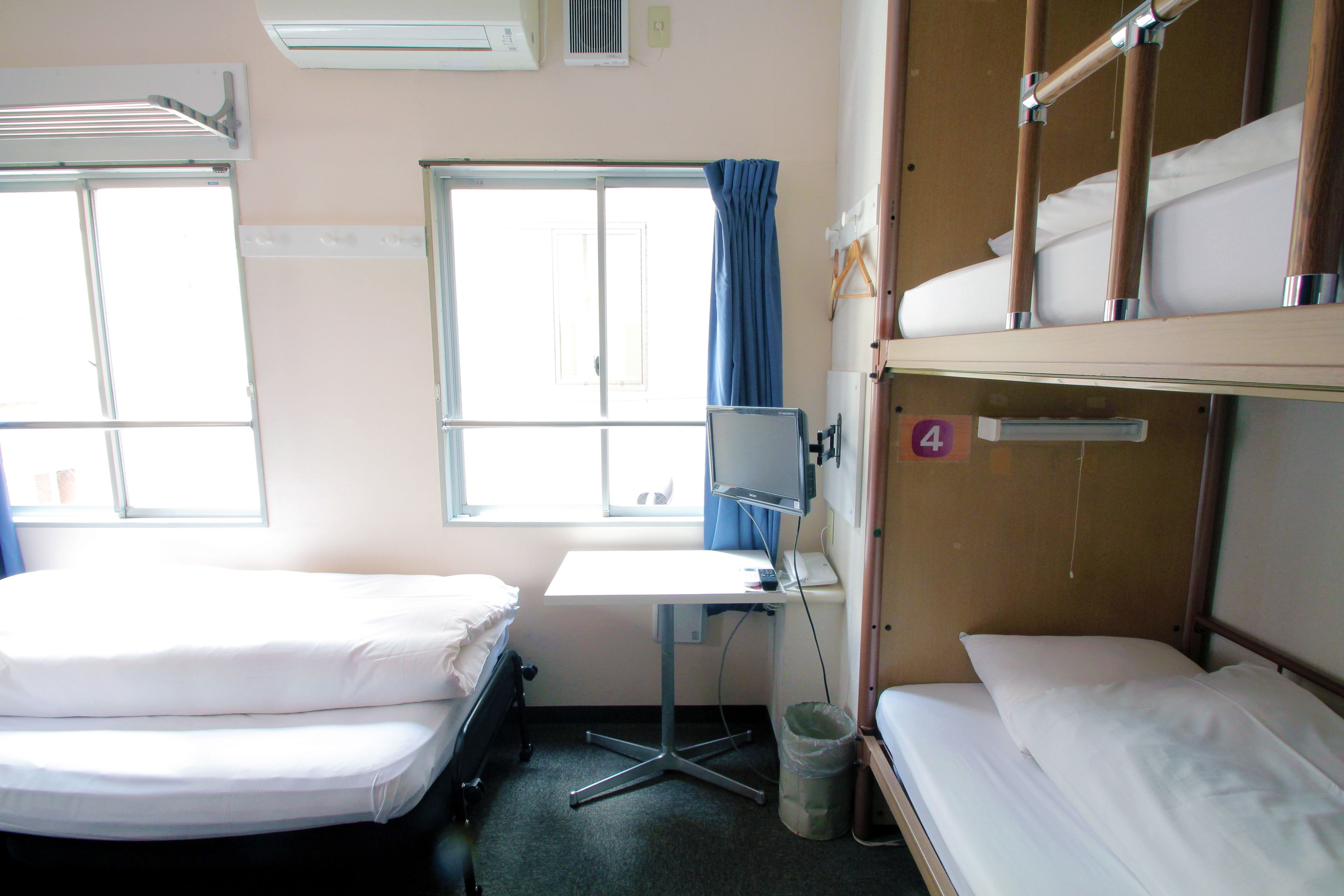 Une chambre d’hôtel avec deux lits simples, un bureau avec un ordinateur, une fenêtre avec des rideaux et un lit superposé.