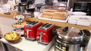 Un bufé de desayuno con tostadoras, una cafetera, un cocedor de arroz y una variedad de panes.