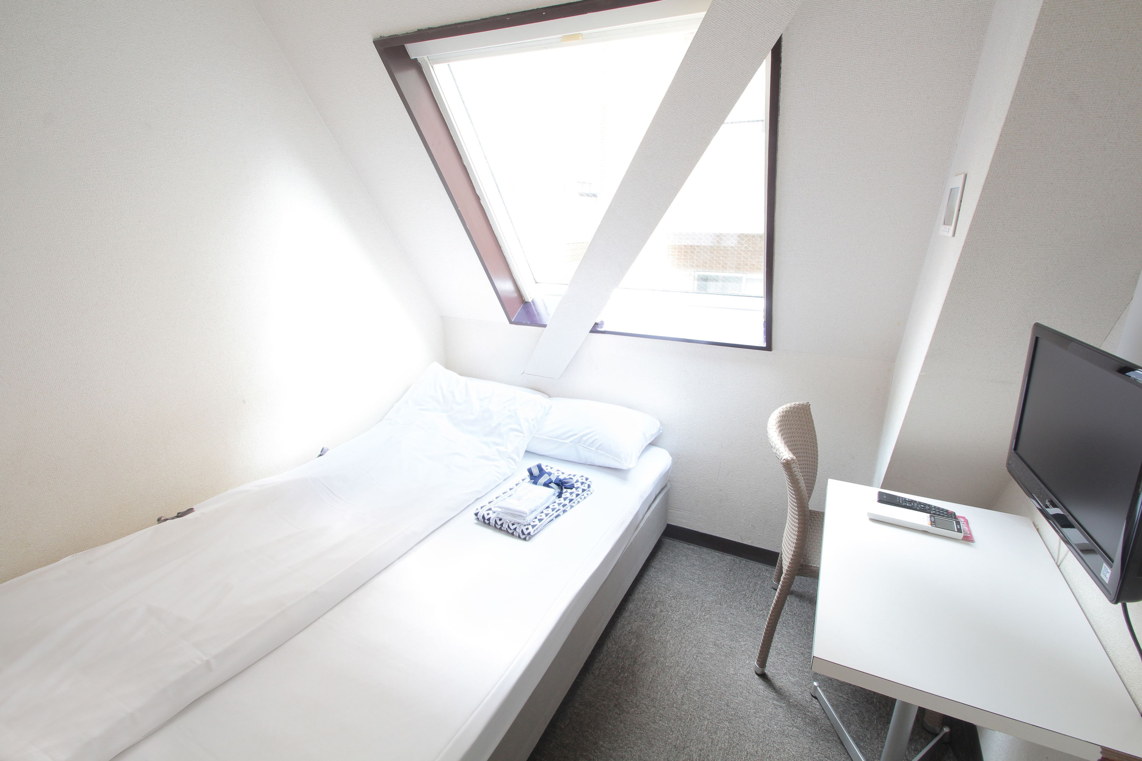 A small, modern room with a single bed, a desk, and a TV.