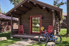 A log cabin with a porch, two red chairs, a blue bicycle, and a small table with flowers. - Turpin Meadow Ranch (Moran)