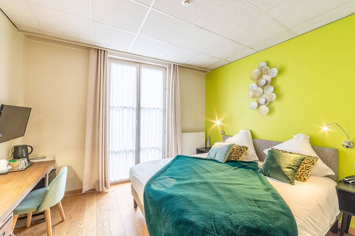 A hotel room with a bed, a desk, a chair, a television, and a window with curtains.