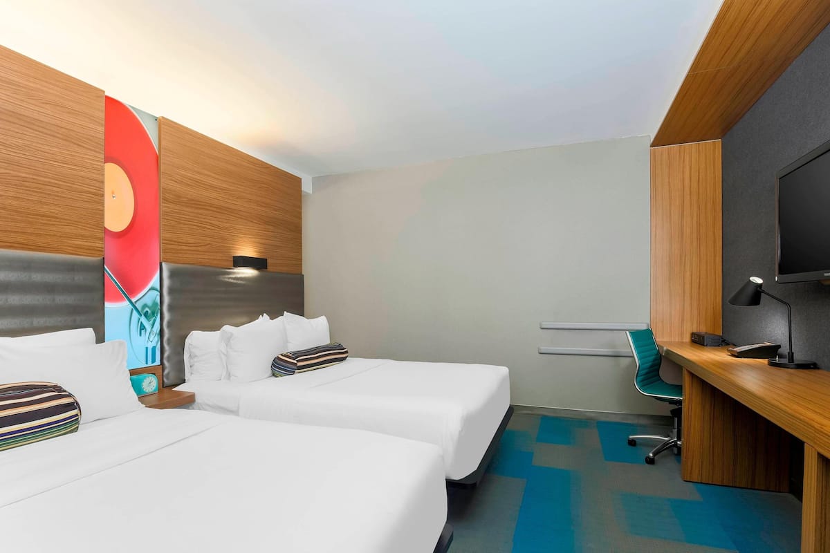 Camera d'albergo con due letti, una scrivania, una sedia, una televisione e un grande quadro astratto appeso al muro.