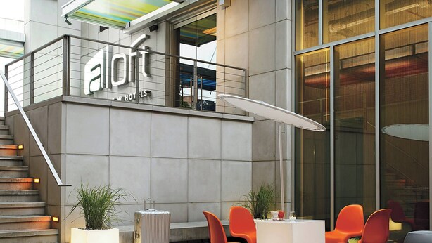 A modern hotel lobby with a staircase, seating area, and a large window. - Aloft by Marriott Harlem (New York)