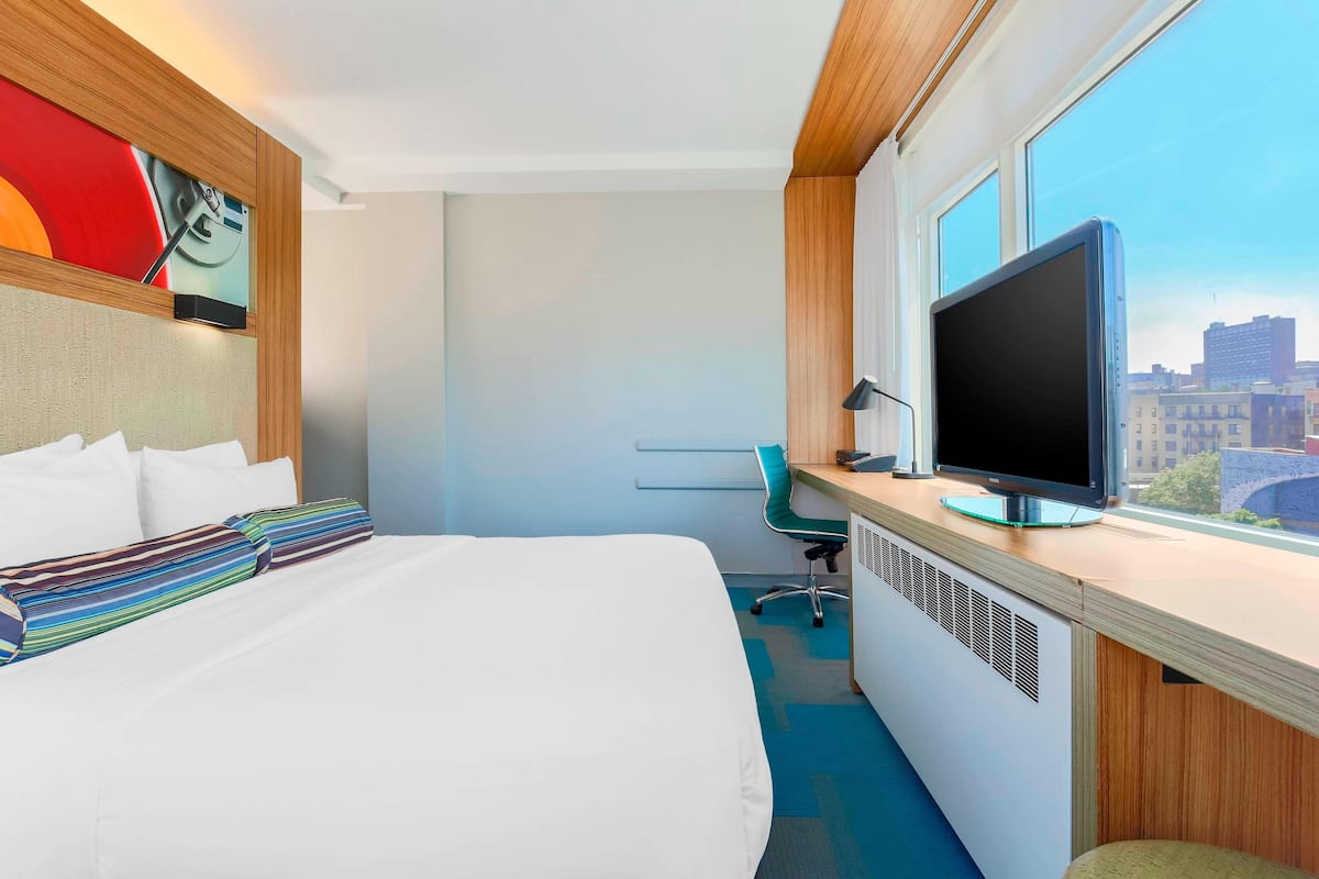 Una camera d'albergo con un letto, una scrivania con un computer, una televisione e una finestra con vista sulla città.