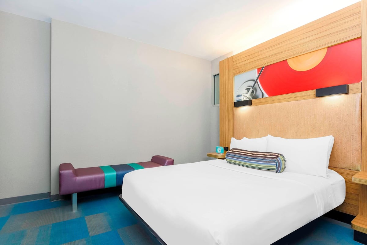 Una camera d'albergo con un letto grande, una testiera in legno, una panca colorata e un'opera d'arte appesa al muro.