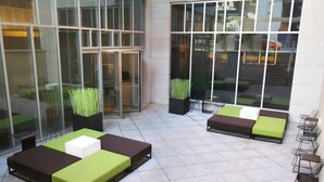 A modern outdoor seating area with green and brown sofas, a white table, and planters with green plants. - Aloft by Marriott Harlem (New York)