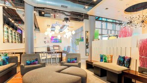 A modern lounge area with seating arrangements, a bar, and a large window providing natural light. - Aloft by Marriott Harlem (New York)