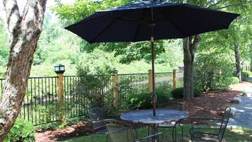 Une table ronde en métal, accompagnée de quatre chaises et d’un grand parasol, dans un cadre de jardin.