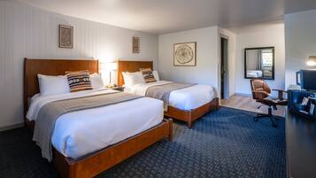 A hotel room with two wooden beds, a desk with a chair, a mirror, and a framed picture on the wall.