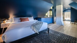A modern bedroom with a large bed, a nightstand, a lamp, and a stone pillar. - Riverhouse by Weekender (Formerly Jack Daniels Inn) (Peterborough)