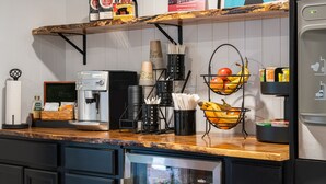 A kitchen with a coffee machine, coffee pods, a fruit basket, and a refrigerator. - Riverhouse by Weekender (Formerly Jack Daniels Inn) (Peterborough)