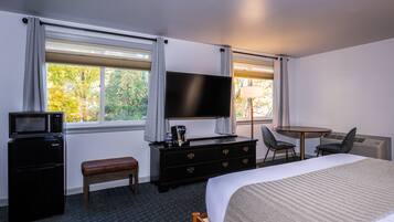 Una habitación de hotel con una cama, un televisor, un escritorio con dos sillas, una mesita, un banco, un microondas y un refrigerador.