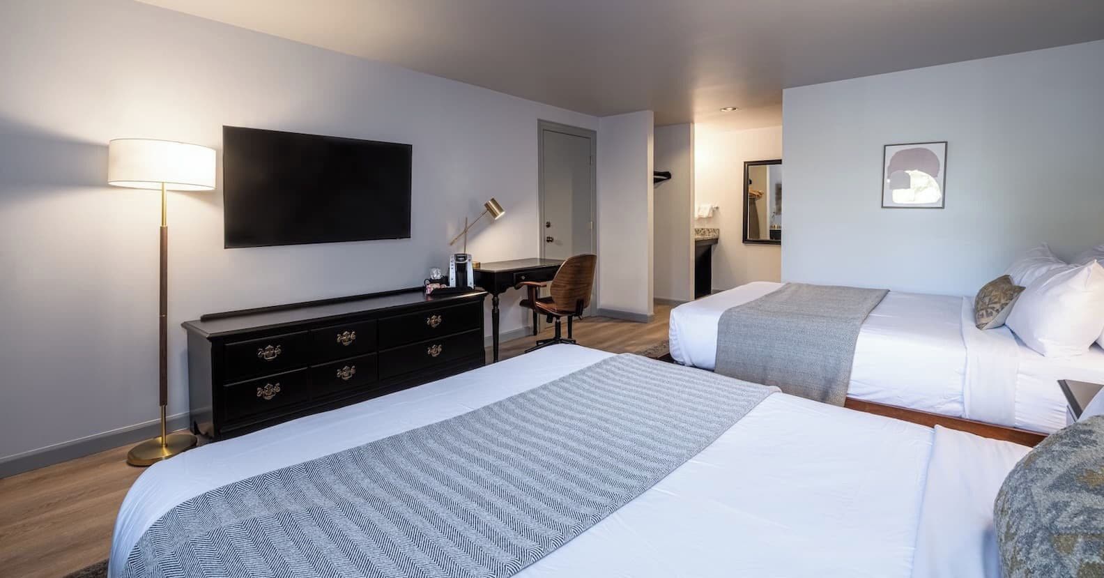 Une chambre d’hôtel avec deux lits, un téléviseur à écran plat, un bureau, une chaise et une lampe.