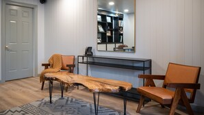 A room with a wooden coffee table, two chairs, a bookshelf, and a large mirror on the wall. - Riverhouse by Weekender (Formerly Jack Daniels Inn) (Peterborough)
