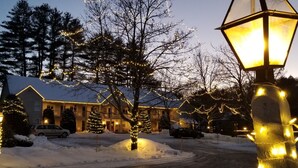 A hotel with a snow-covered driveway, Christmas lights, and a large tree in front. - Riverhouse by Weekender (Formerly Jack Daniels Inn) (Peterborough)