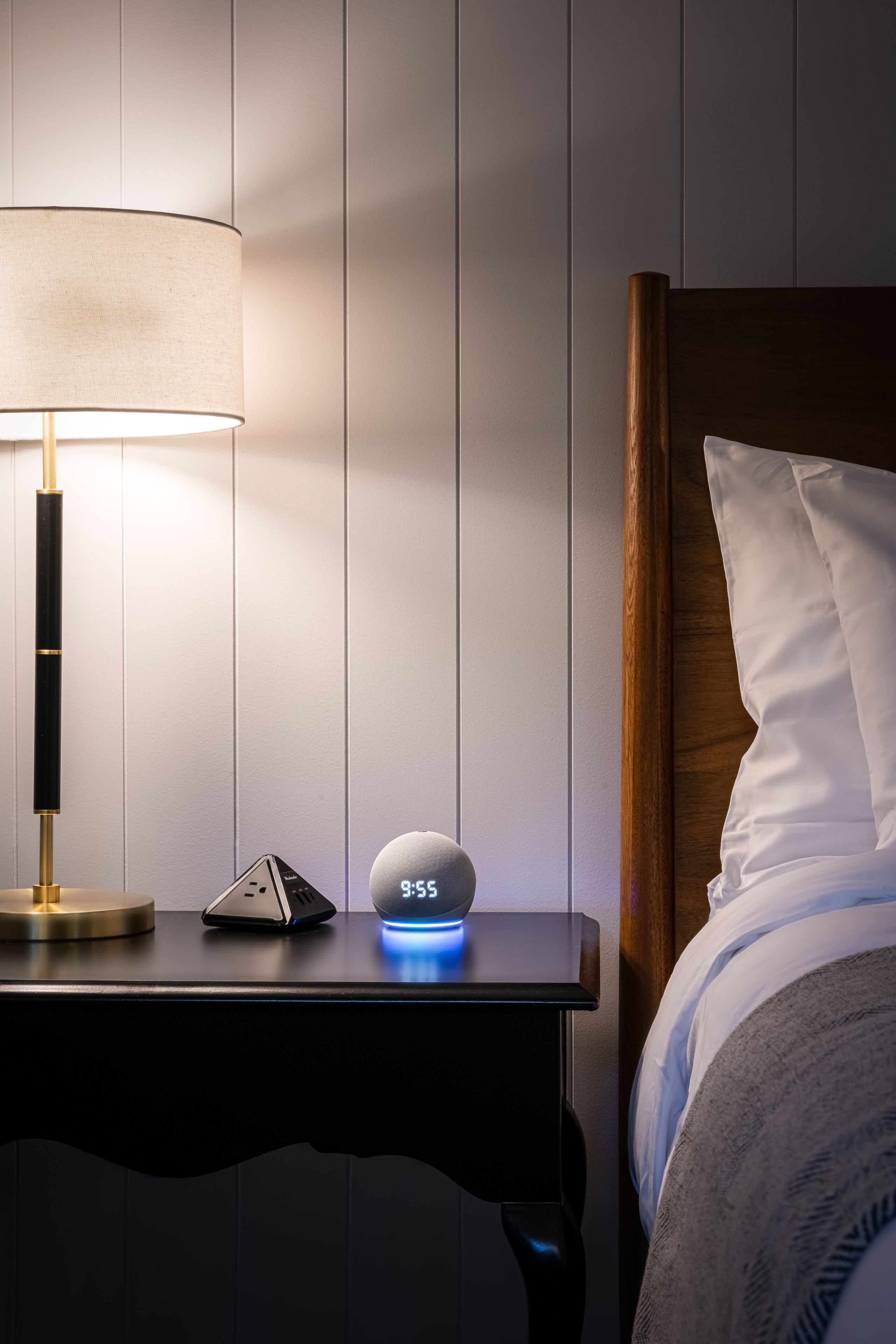 A bedside table with a lamp, a digital clock, and a remote control.