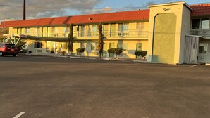 A motel with a red roof, a covered parking area, and a clear sky. - Ramblin Rose Motel (Kingman)
