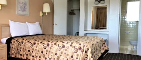 A hotel room with a bed, bedside lamps, a mirror, a wardrobe, and a bathroom with a toilet and sink.