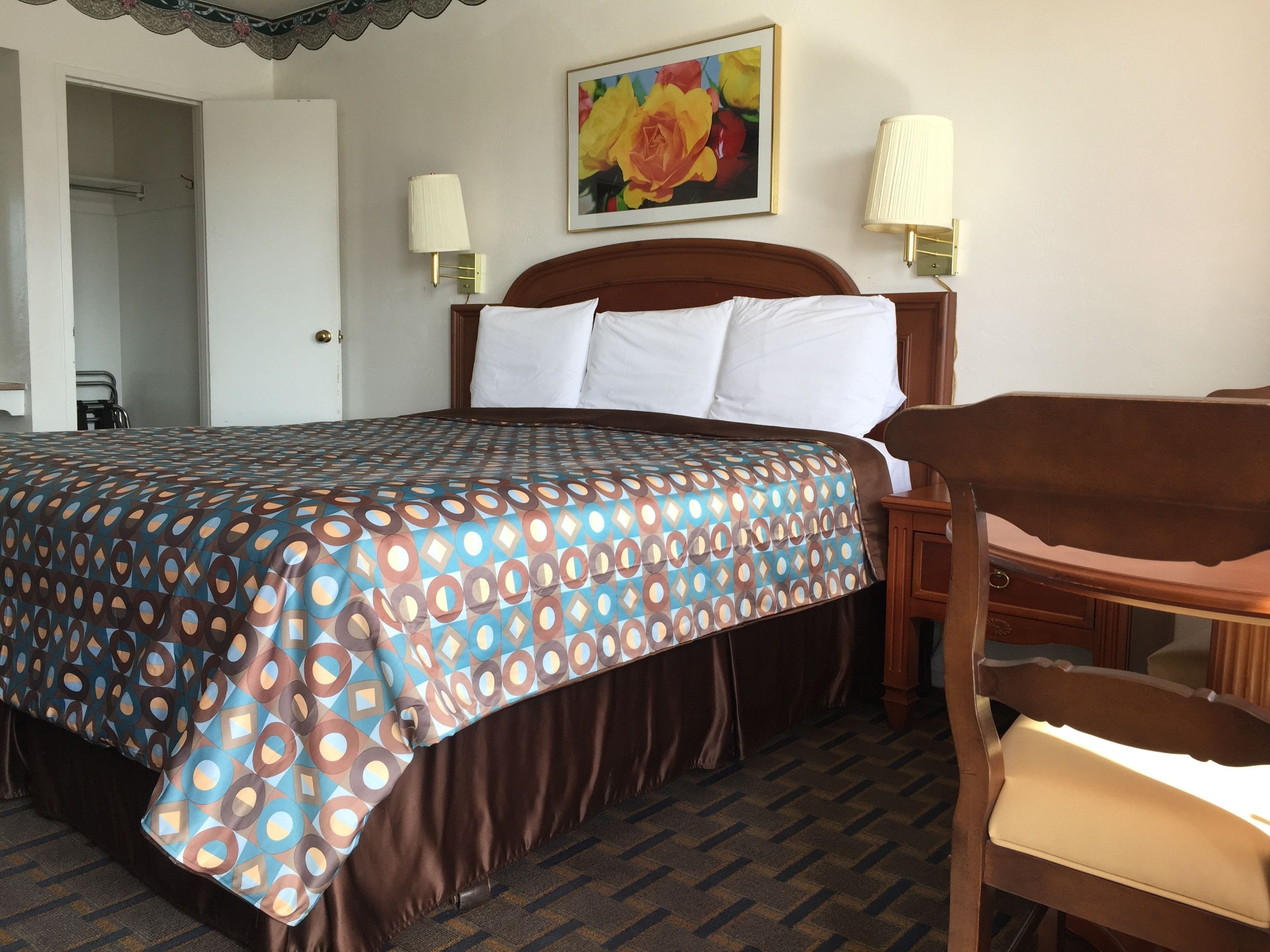 A hotel room with a large bed, two bedside lamps, a wooden headboard, a chair, and a painting on the wall.