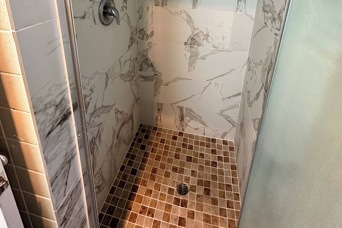 Une douche aux murs et au sol recouverts de carreaux de marbre.