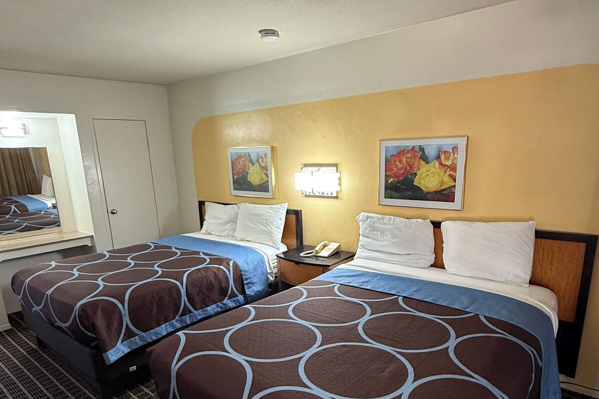 Une chambre d’hôtel avec deux lits, un bureau, un miroir et deux lampes fixées au mur.