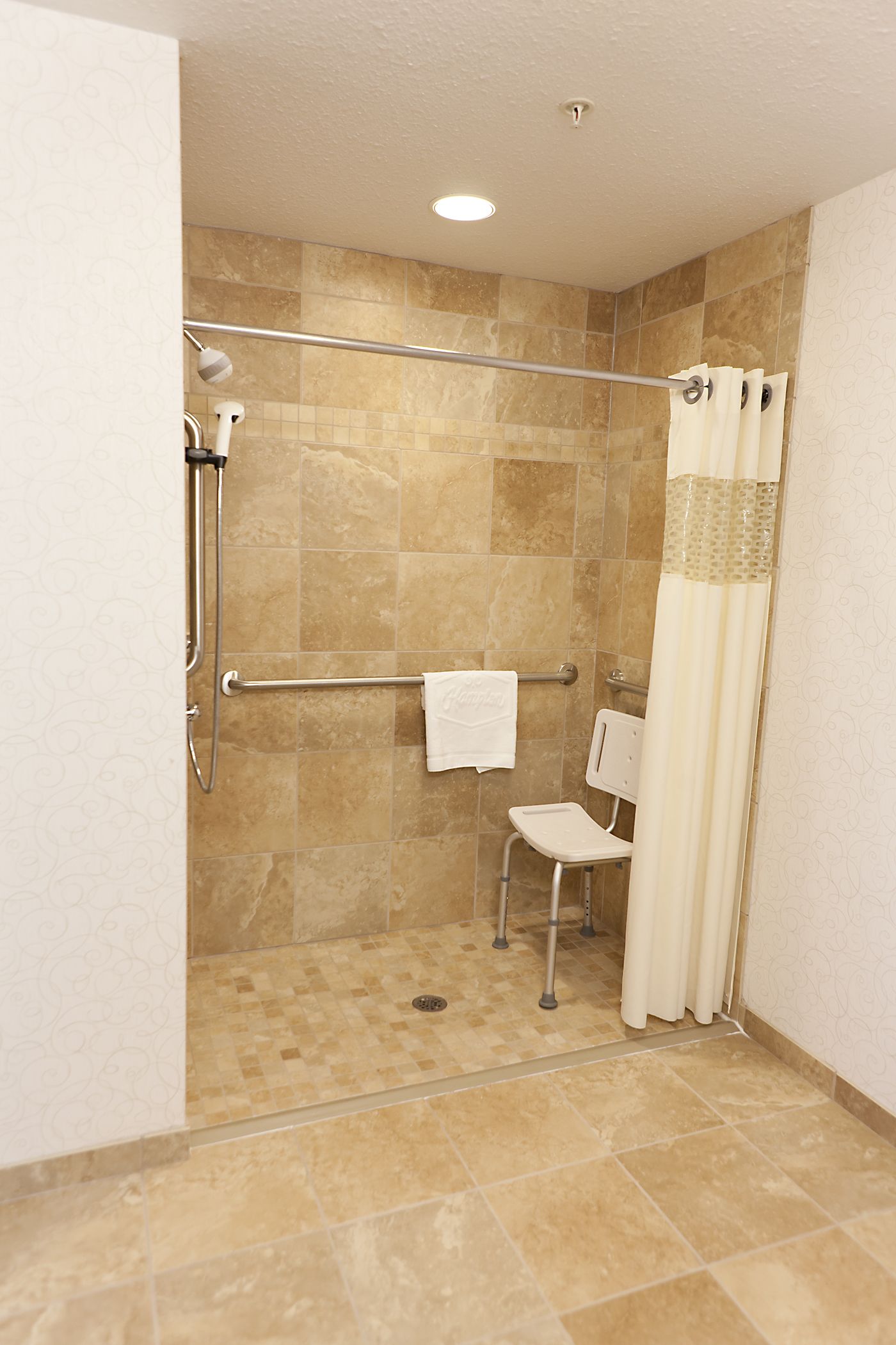 A shower area with a glass door, a towel rack, and a wheelchair-accessible bench.