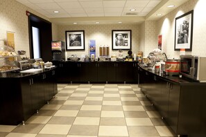 Zona de desayuno de hotel con piso a cuadros, barra de buffet y cuadros en las paredes.