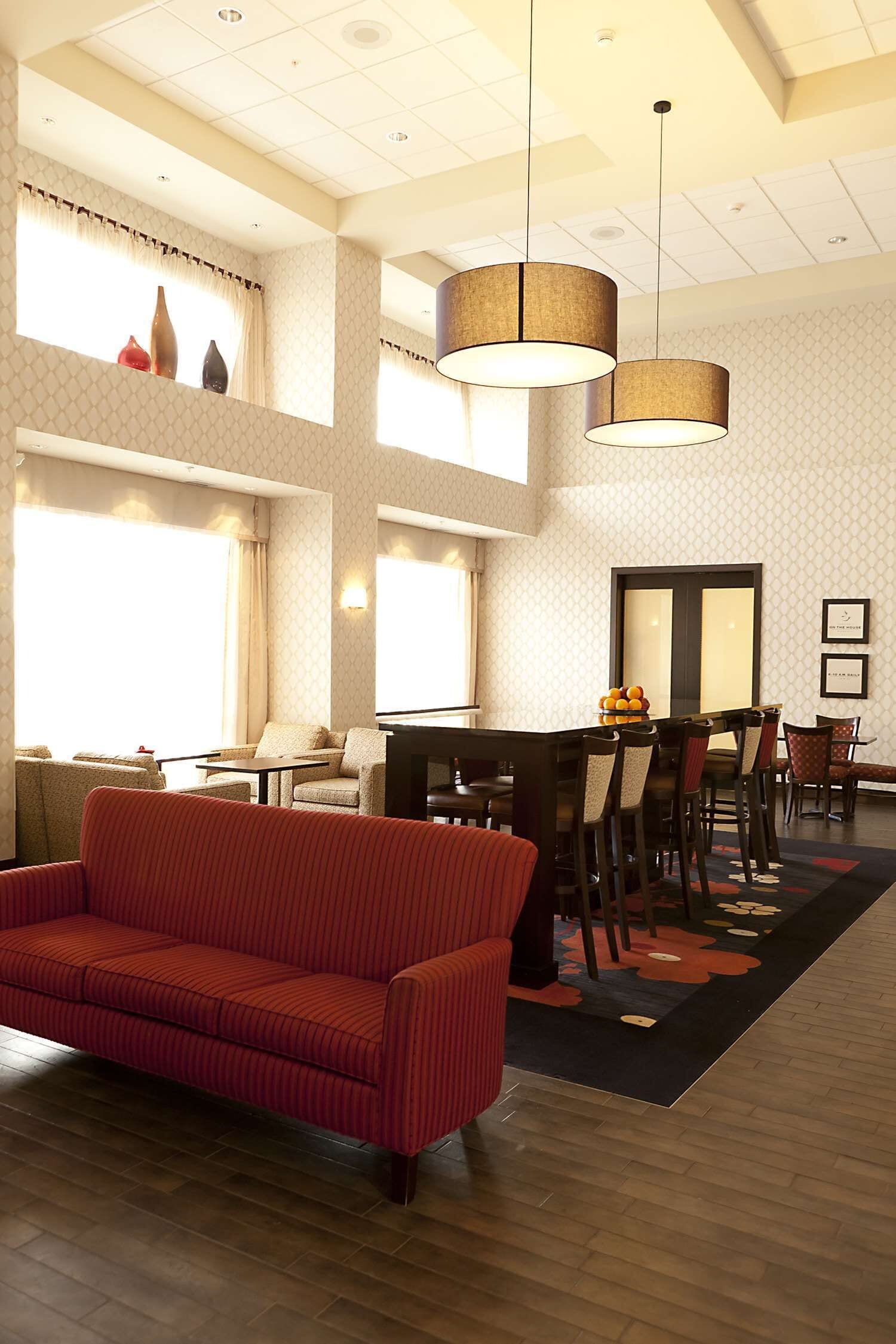 Un hall d’hôtel spacieux avec un grand canapé, un coin repas comprenant une table et des chaises, et une grande fenêtre avec des rideaux.